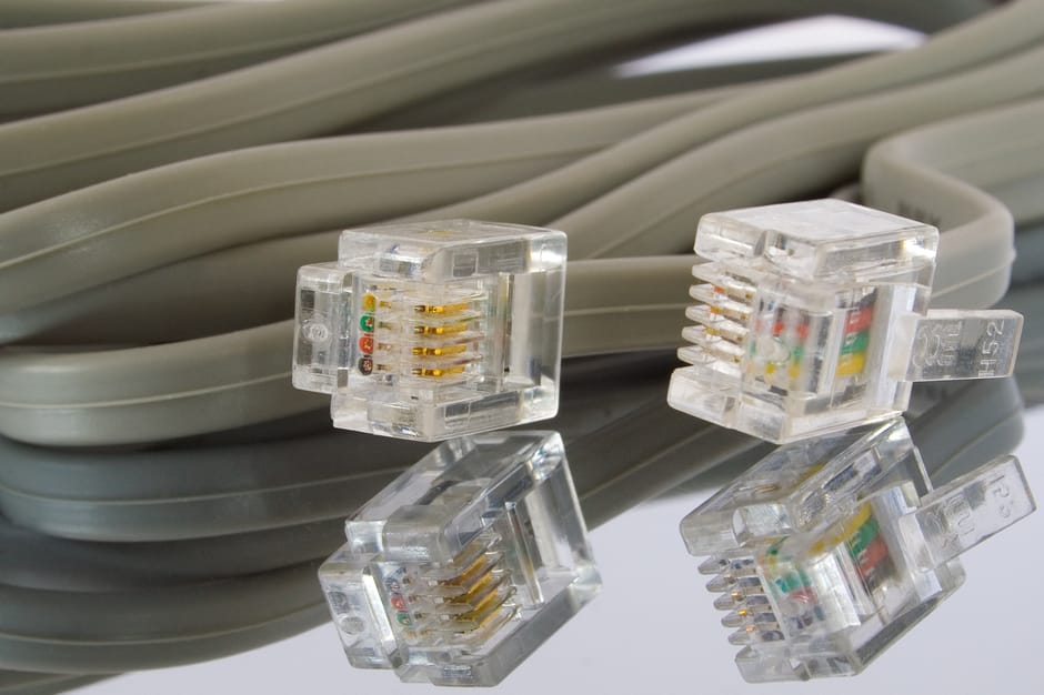 Close-up image showing a coiled grey Ethernet cable with four clear plastic RJ45 connectors, each containing gold-plated contacts and small colored internal wires visible through the transparent casin